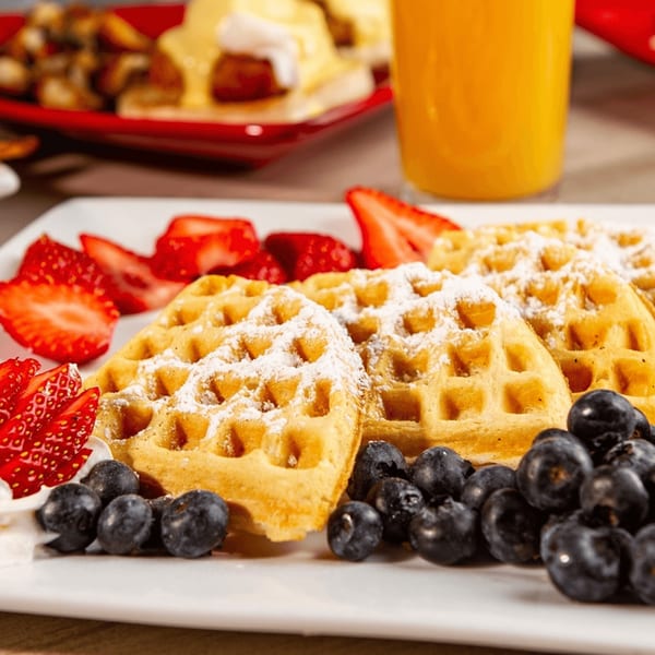 Golden waffles dusted with powdered sugar, fresh strawberries, and blueberries on a white plate.
