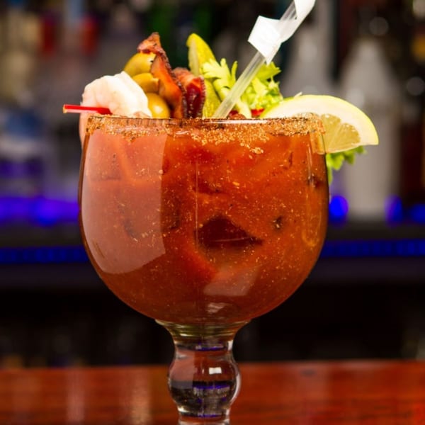A Bloody Mary cocktail with shrimp, bacon, olives, celery, and a lemon slice.
