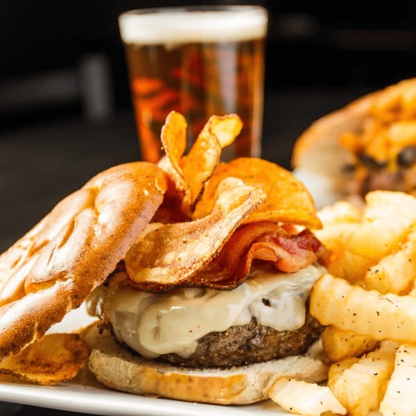 A Village Idiot Pub burger with melted cheese, bacon, chips, fries, and a beer.