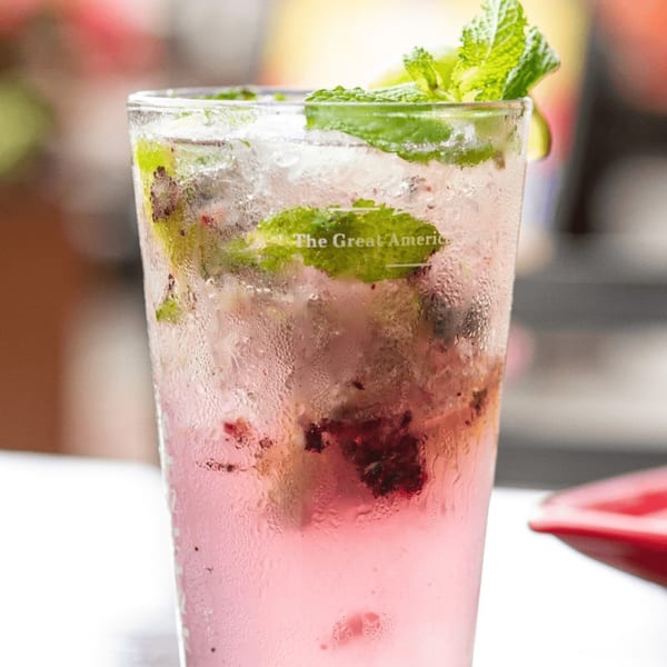 A frosty glass of pink mojito with muddled berries, mint leaves, and ice, on a white table.