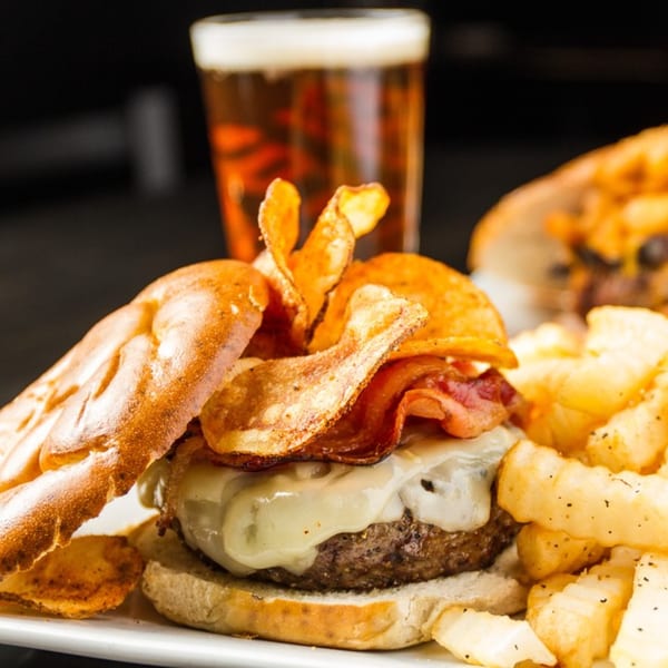 A Village Idiot Pub burger with melted cheese, bacon, chips, fries, and a beer.