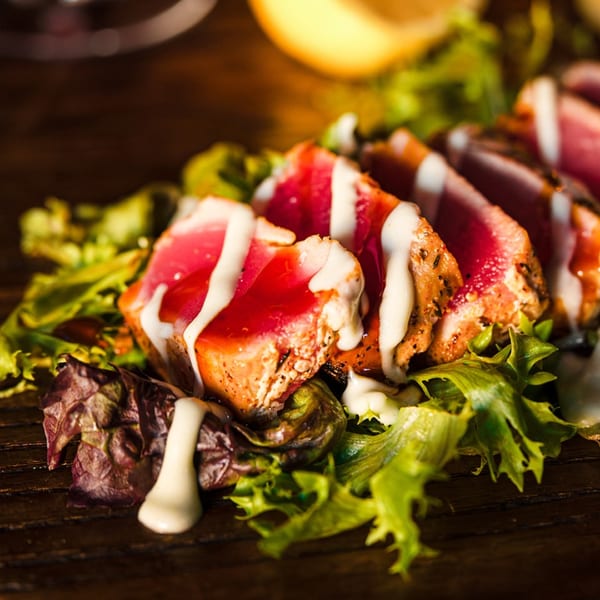 Seared tuna slices with white sauce drizzle on a bed of mixed greens at Village Idiot Pub.